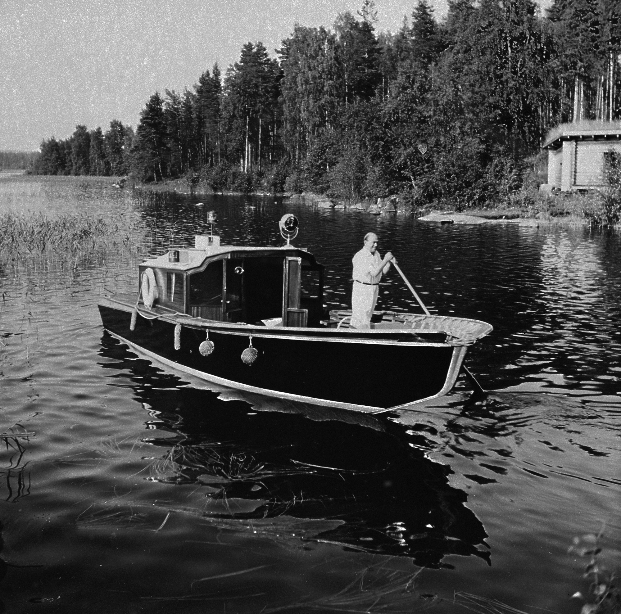 Alvar Aalto ohjaa venettään Muuratsalon rannassa 1950-luvulla. Alvar Aalto and the Nemo propheta in patria boat at Muuratsalo. Photo Pellervo Oksala, Alvar Aalto Foundation. AR 53-1